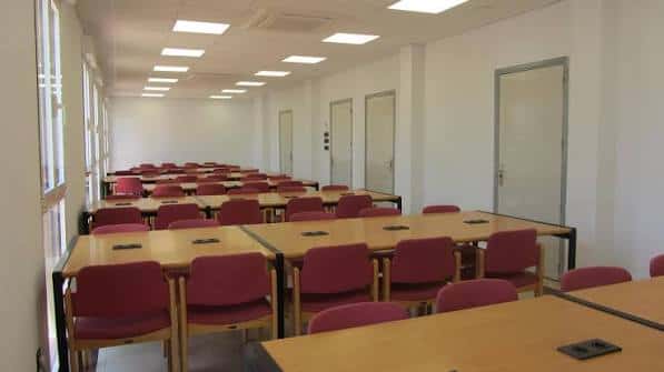 Aula amplia y luminosa de la UNED Elche, equipada con mesas y sillas rojas listas para eventos o clases