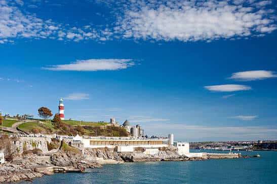 Vista costera de Plymouth Hoe con el faro y el Plymouth Pavilions bajo un cielo azul