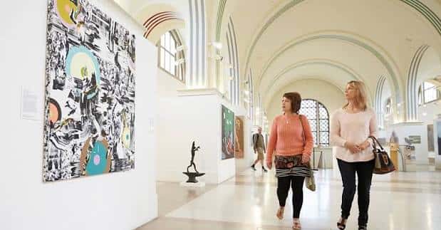 Interior de la galería con visitantes observando obras de arte moderno en salas amplias y luminosas