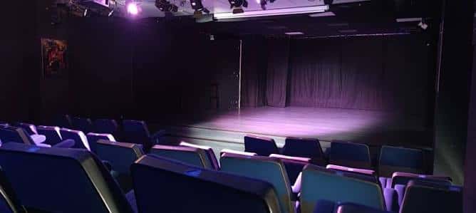 Interior del auditorio de La Caverna del Brujo con escenario iluminado y butacas