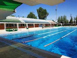Piscina olímpica con carriles marcados y gradas bajo toldo verde