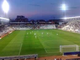 Estadio de fútbol del complejo deportivo durante un partido nocturno con iluminación artificial