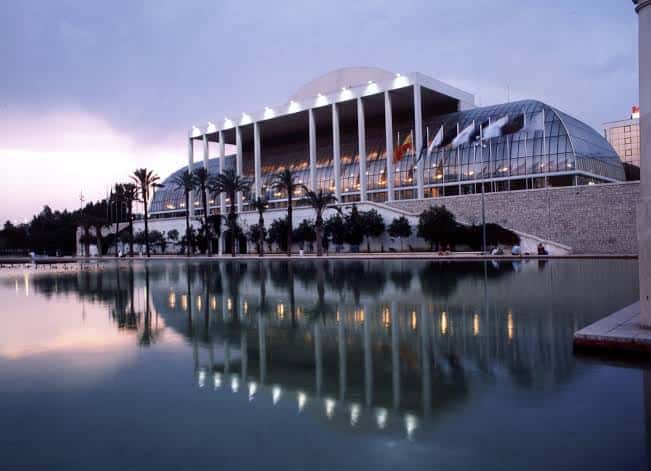Fachada del Palau de la Música al atardecer con reflejo en el agua y banderas ondeando