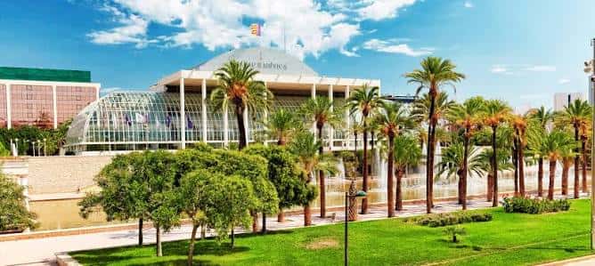 Panorámica del Palau de la Música con jardines, palmeras y fuentes activas en un día soleado