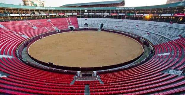 Vista panorámica del coso taurino con gradas rojas y arena central vacía