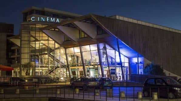 Fachada nocturna del Harbour Lights Picturehouse iluminada con luces azules y letrero 'CINEMA'