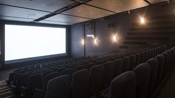 Interior del auditorio con butacas grises, pantalla blanca y escalera lateral