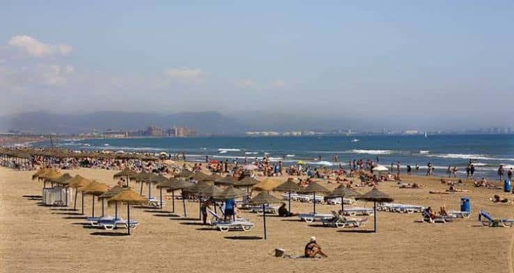 Playa de la Malvarrosa con sombrillas de paja y bañistas disfrutando del sol