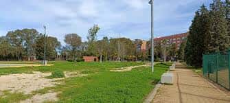 Área verde del parque con sendero y edificios residenciales al fondo