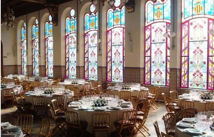 Sala de banquetes con grandes ventanales de vidrieras y mesas decoradas