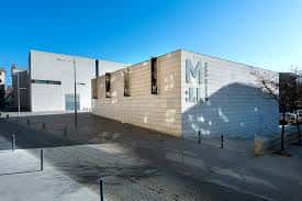 Exterior del edificio del museo bajo cielo azul, mostrando su arquitectura moderna y el logo 'MUSEU'