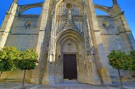 Entrada frontal de la iglesia con portada ornamentada y árboles a los lados