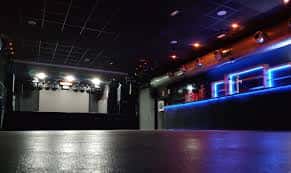 Interior del club con escenario, luces de neón y barra iluminada