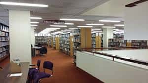 Vista panorámica del interior de la biblioteca con múltiples pasillos de libros y mesas de estudio