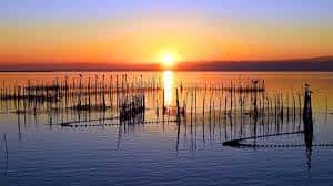 Atardecer dorado sobre la laguna con estructuras de pesca tradicionales y cielo despejado