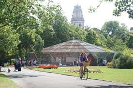 Estructura de cristal en el parque con visitantes y ciclistas en primer plano