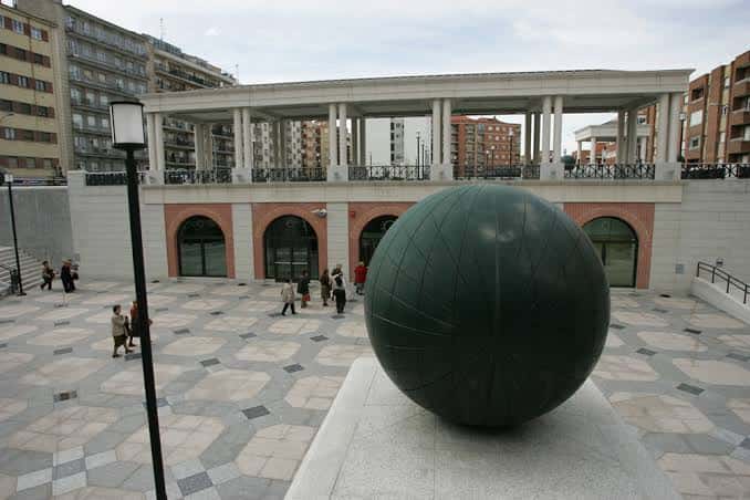 Plaza exterior del museo con escultura de esfera y arquitectura moderna