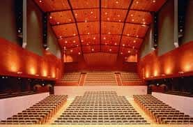 Interior del auditorio con gradas curvas, techo acústico y asientos en tonos cálidos