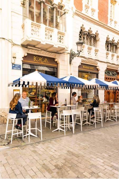 Terraza exterior de Borgia Winebar con clientes disfrutando bajo sombrillas azules y blancas