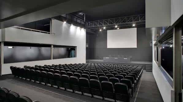 Aula magna con butacas negras y pantalla de proyección