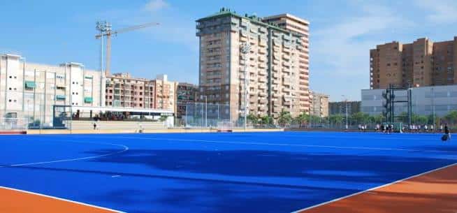 Campo de hockey con césped sintético azul y gradas al fondo