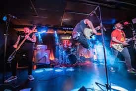 Banda tocando en vivo en el escenario del Loco Club con iluminación azul y roja