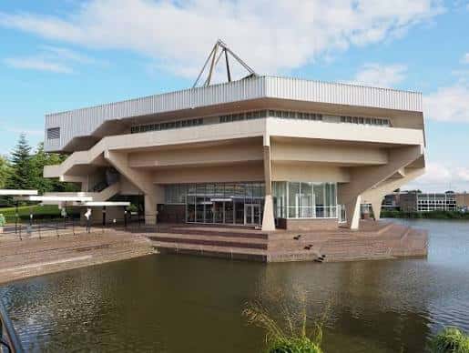 Vista exterior del Central Hall de la Universidad de York con su arquitectura brutalista y reflejo en el lago