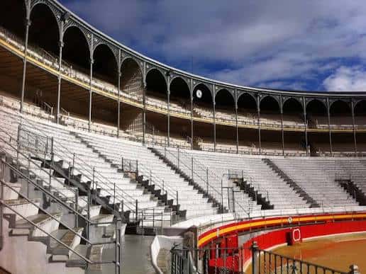 Interior de la Plaza de Toros de Granada con gradas blancas, estructura metálica y arena, sin público ni eventos en curso