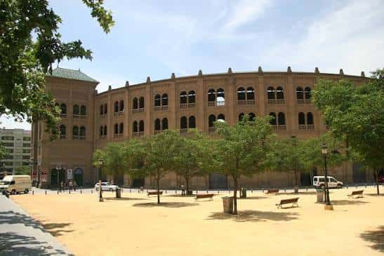 Vista exterior de la Plaza de Toros de Granada con su fachada de ladrillo y arcos, rodeada de árboles y plaza