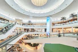 Interior del Centro Comercial Saler con atrio circular, escaleras mecánicas y palmeras decorativas
