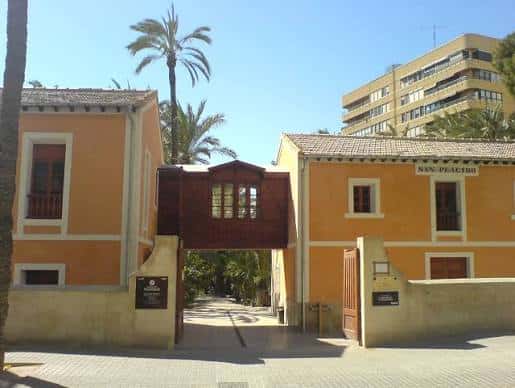 Entrada principal del Museo del Palmeral con fachada amarilla y puente de madera