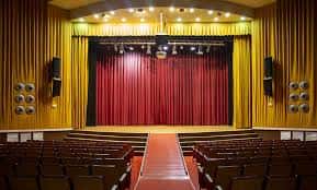 Interior del Teatro La Plazeta con escenario, cortina roja y butacas de madera