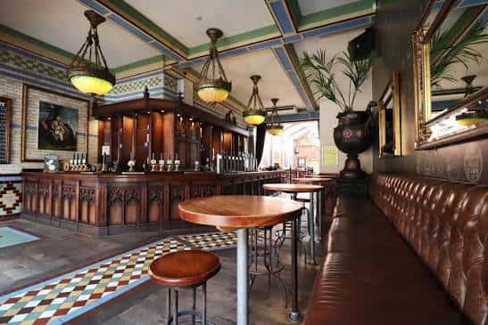 Interior del bar con barra de madera, techos decorados y asientos de cuero