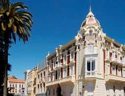 Ángulo elevado de la torre y fachada del Palacio Aguirre bajo cielo azul, con palmera en primer plano