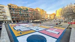 Plaza con mural colorido en el suelo y ambiente urbano con personas caminando