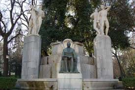 Plano medio del monumento mostrando la estatua central y las figuras laterales entre árboles