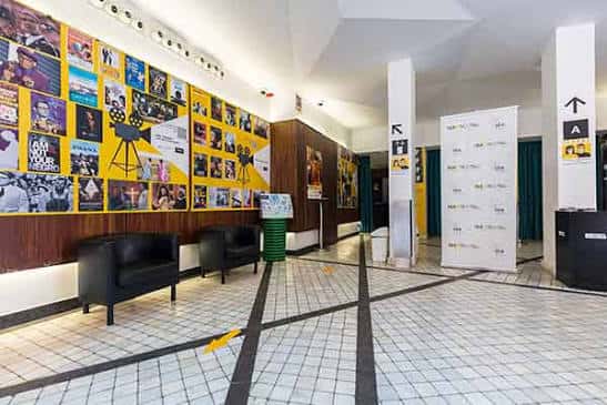 Interior del vestíbulo de la Filmoteca con paredes decoradas con carteles de cine y zona de espera