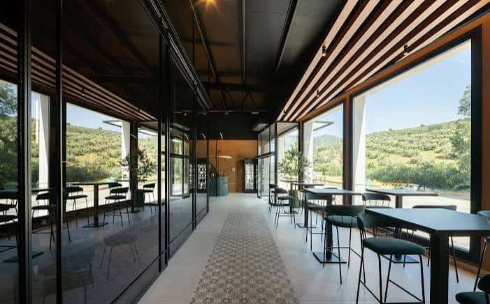 Interior del restaurante con mesas altas y grandes ventanales con vistas al paisaje