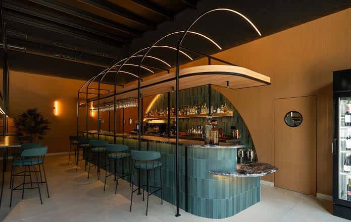 Bar interior con diseño curvo, azulejos verdes y iluminación arquitectónica