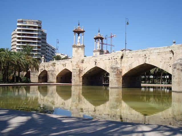 Vista frontal del Puente de Serranos reflejado en el agua del cauce del Turia