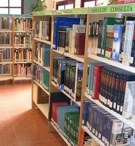 Interior de la biblioteca con estanterías de libros y señalización de secciones
