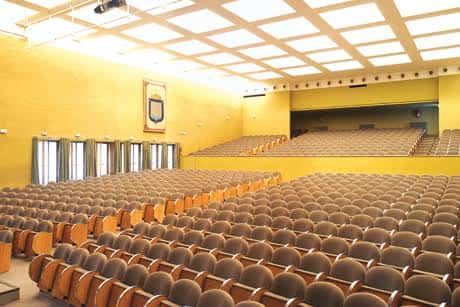 Interior del auditorio con iluminación amarilla y escudo municipal en la pared