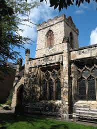 Vista exterior de la Holy Trinity Church en York, mostrando su torre de piedra y ventanas góticas bajo un cielo azul