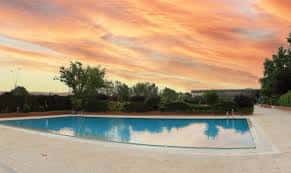 Piscina municipal al atardecer con cielo anaranjado y entorno natural
