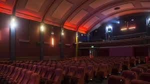 Interior del auditorio con butacas rojas, iluminación cálida y techo abovedado