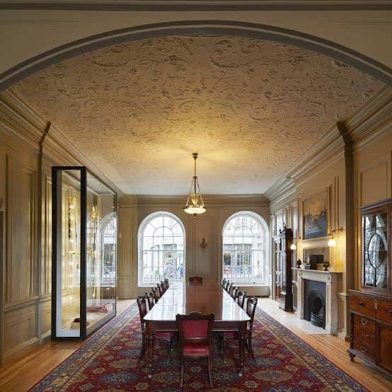Sala de banquetes con mesa larga, techos ornamentados y ventanas arqueadas, apta para cenas formales