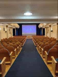 Sala de proyección con pantalla encendida y butacas de madera dispuestas en filas
