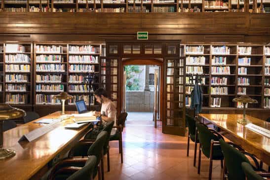Interior de la biblioteca con estanterías de madera y mesas de lectura