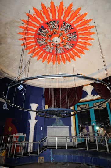 Interior del auditorio con una gran instalación artística en forma de sol naranja colgando del techo, ideal para eventos culturales