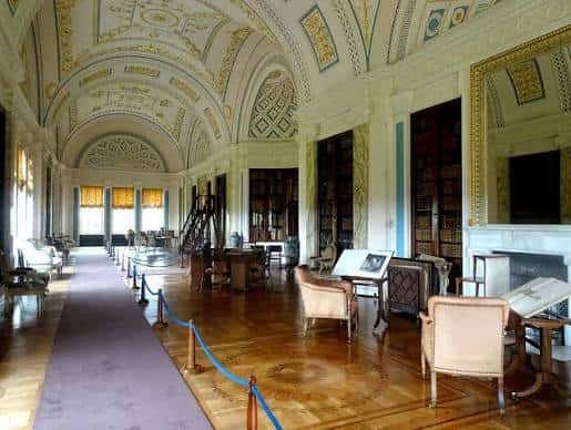 Interior de la biblioteca histórica con techos decorados, estanterías de madera y mobiliario clásico